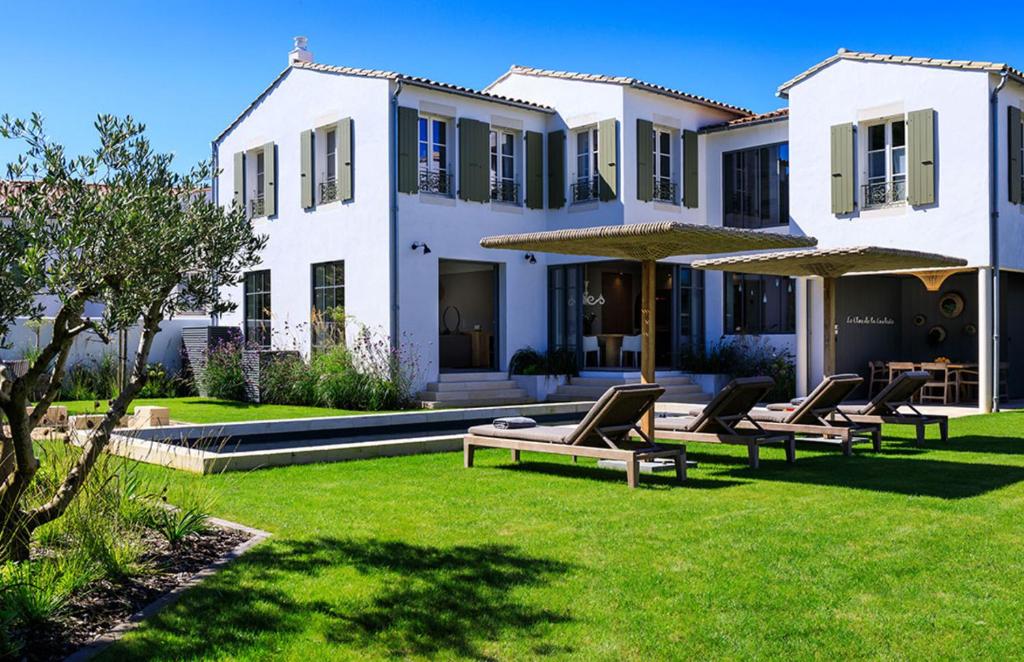 une maison avec des chaises et des parasols dans une cour dans l'établissement Le Clos de la Corderie, à La Flotte