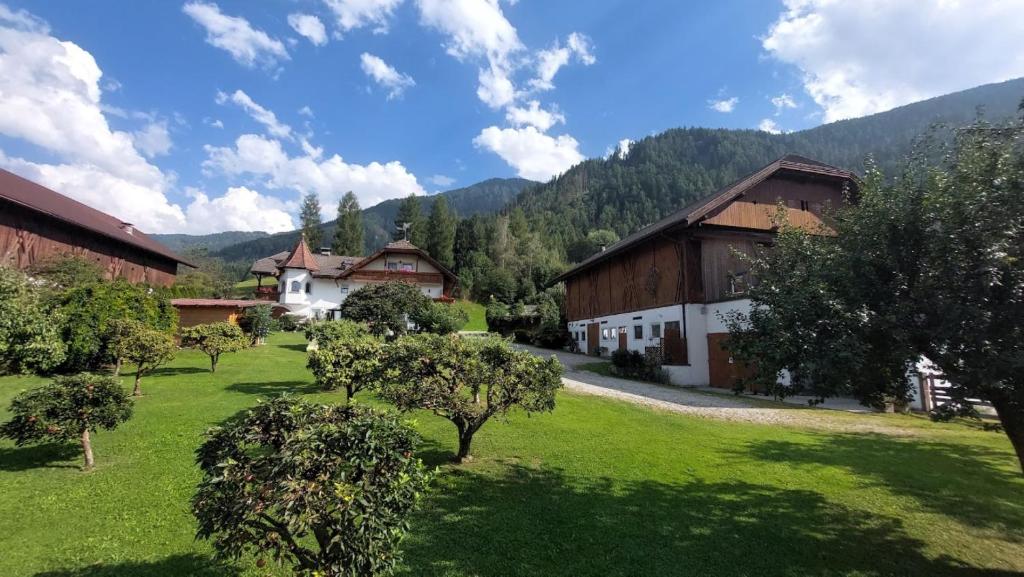 un patio verde con edificios, árboles y montañas en Mair am Hof - Farm - Maso - Bauernhof, en San Lorenzo di Sebato
