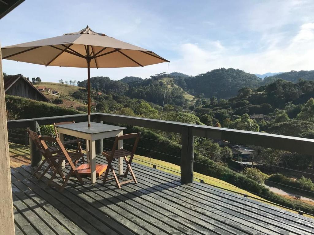 une table et des chaises sur une terrasse avec un parasol dans l'établissement Chalé Serra do Luar, à Santo Antônio do Pinhal