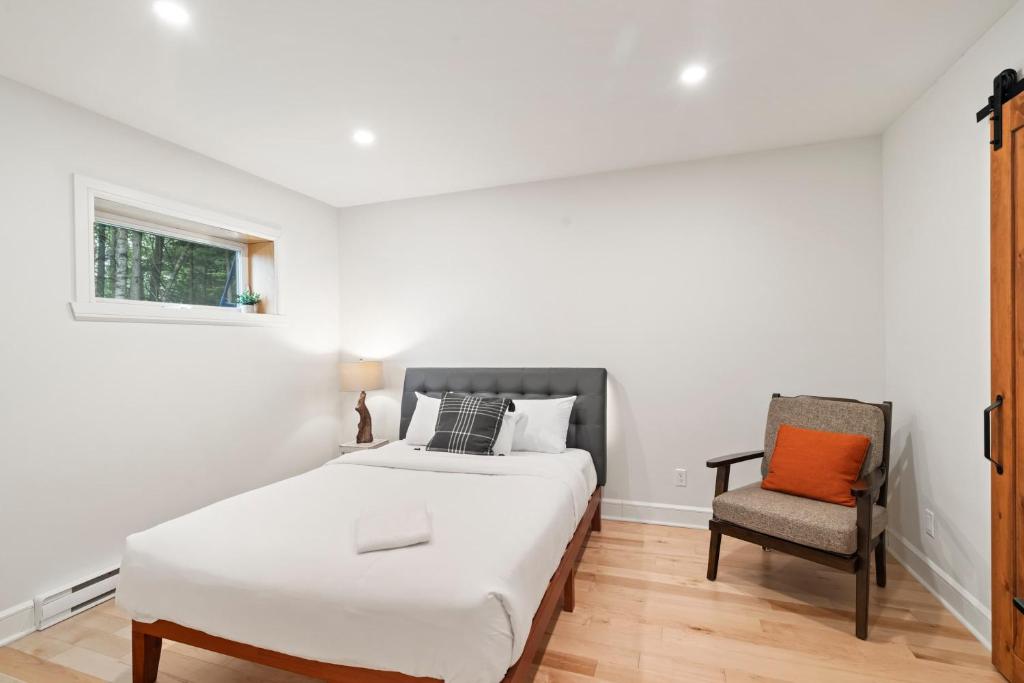 a white bedroom with a bed and a chair at Chalet La Colline in Labelle