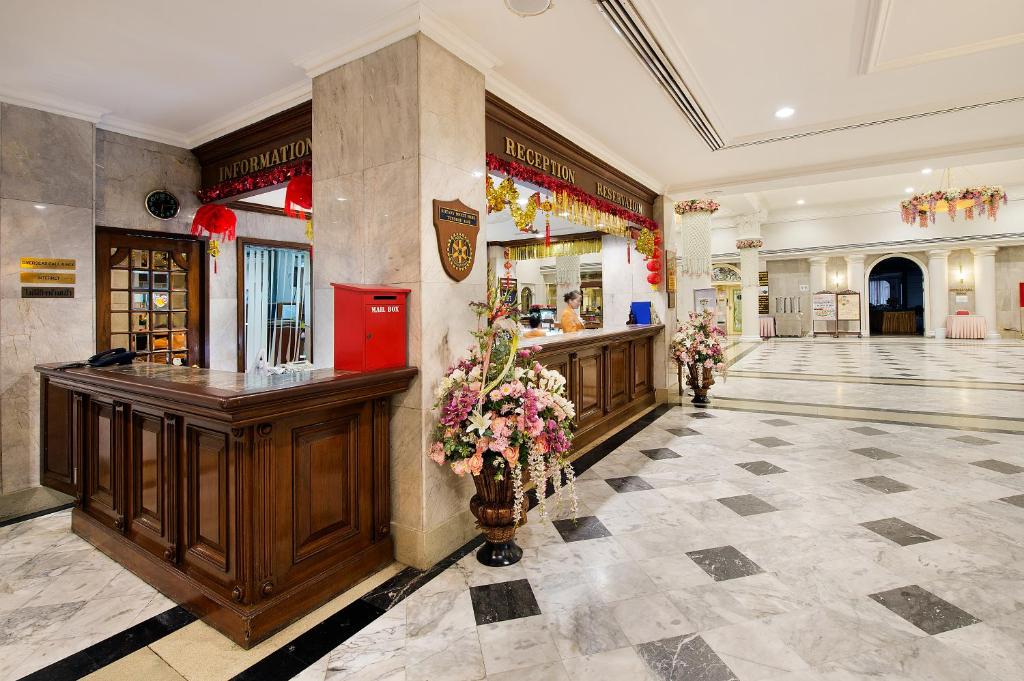 A grand hotel lobby with a reception counter, information desk, marble flooring, and floral arrangements.