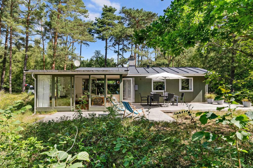 a green tiny house with a patio in the woods at Cottage In Peaceful Surroundings In Vester Sømark in Vester Sømarken