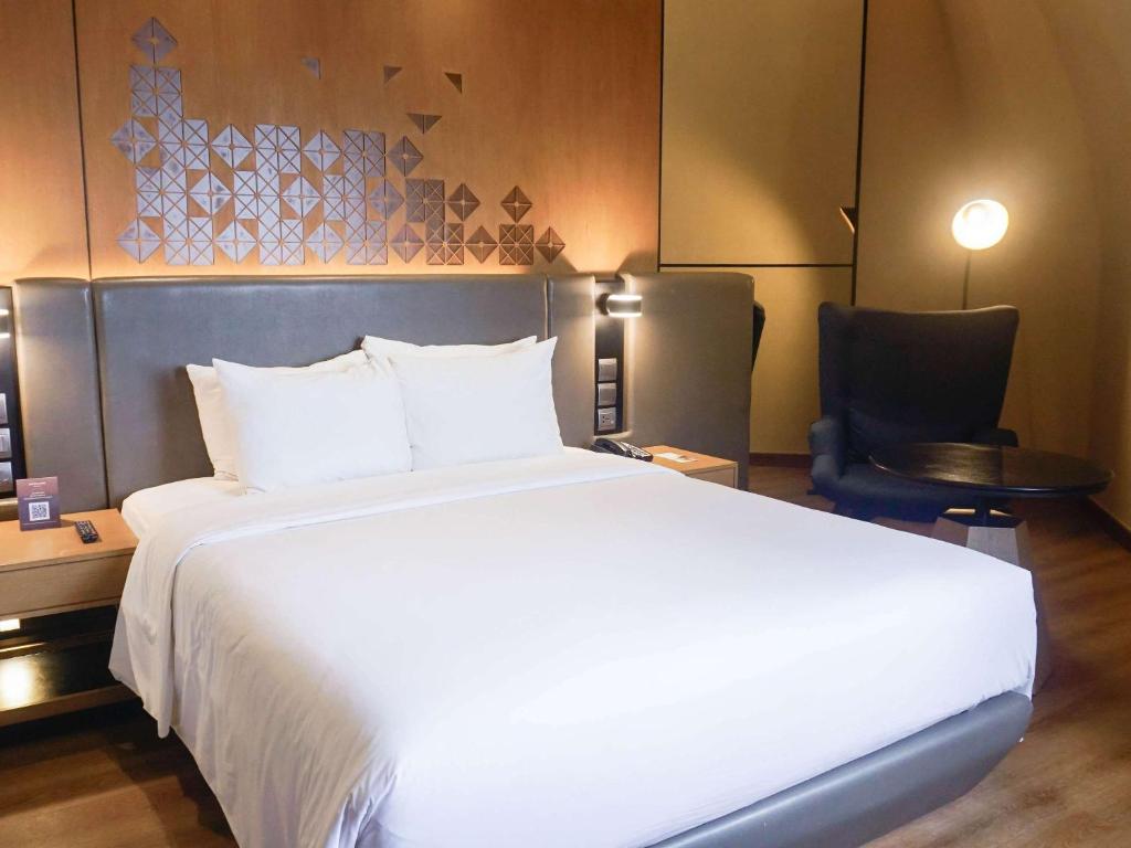 a bedroom with a large white bed and a chair at Mercure Jakarta Batavia in Jakarta