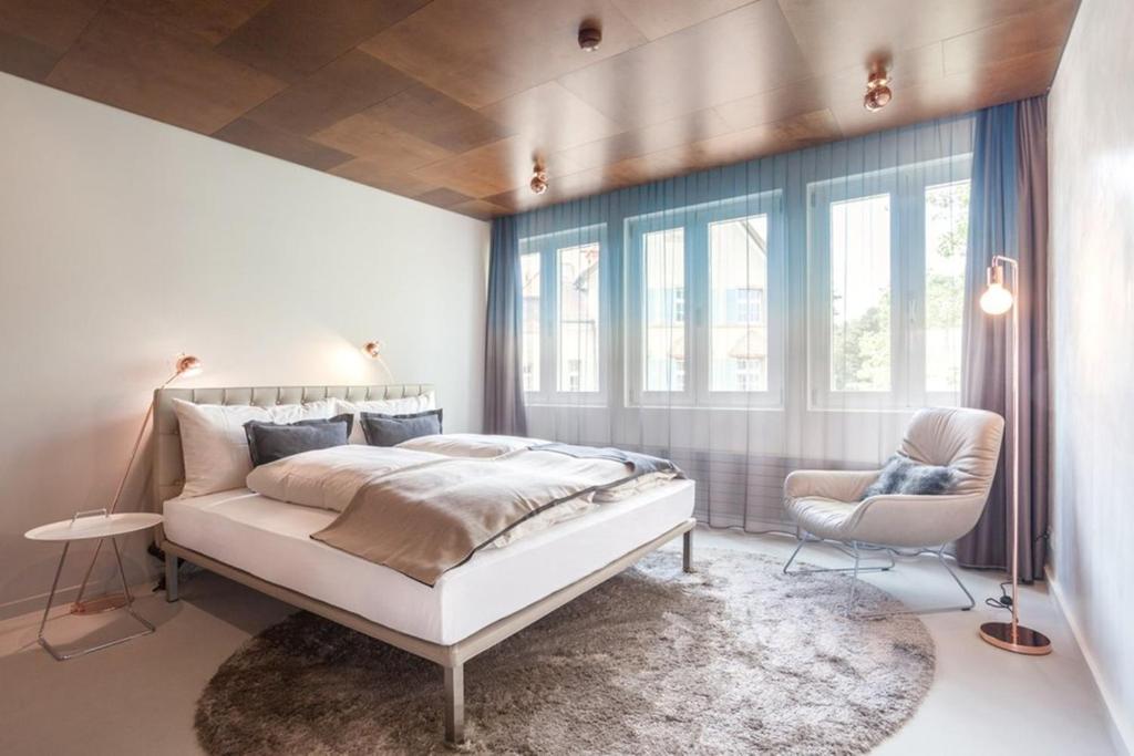 a bedroom with a bed and a chair and windows at EMA House Hotel Suites in Zurich