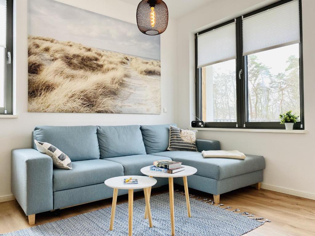 a living room with a blue couch and two tables at Ferienwohnung Windflüchter Parkvillen Carlota und Candela Baabe in Baabe
