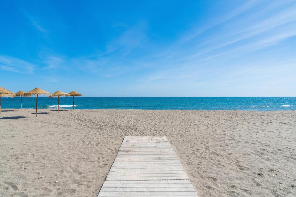 a wooden pathway on a beach with umbrellas and the ocean at Rincón Playa, terraza y piscina in Rincón de la Victoria