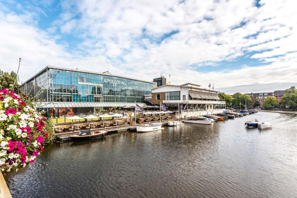 a large building with boats docked next to a river at Apollo Hotel Amsterdam, a Tribute Portfolio Hotel in Amsterdam