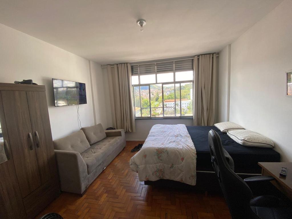 Un dormitorio con una cama y un sofá y una ventana. en Apartamento Centro de São Lourenço - com vista para o parque das águas, en São Lourenço