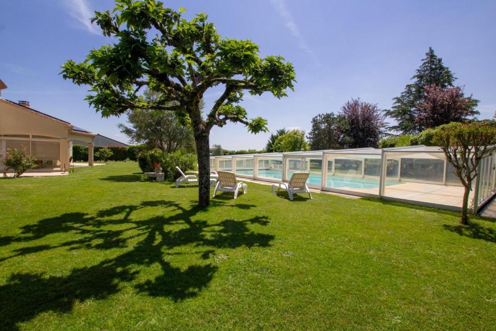 un patio verde con un árbol y una piscina en Kaz a muscadelle, en Saint-Laurent-des-Vignes