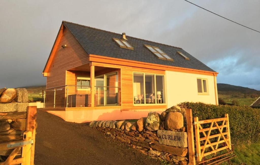 una piccola casa con una recinzione in pietra di fronte di Curlew Cottage a Gatehouse of Fleet