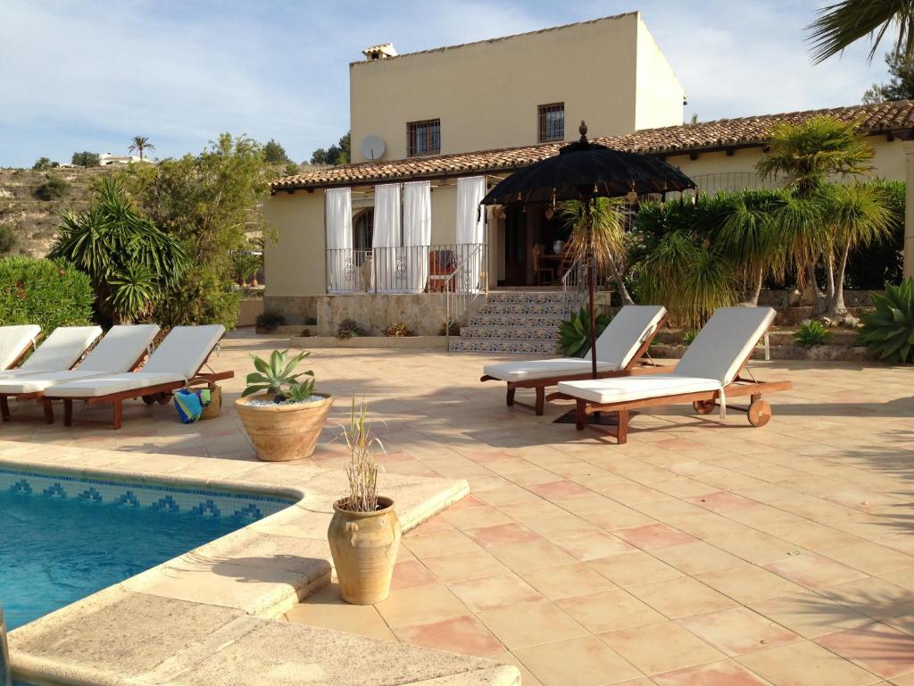 un grupo de tumbonas y una sombrilla junto a la piscina en Finca la Jarra, en Benitachell