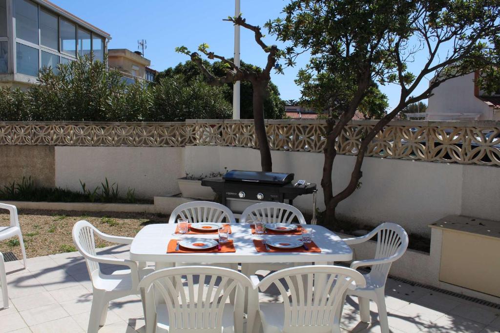 une table avec des chaises blanches et un barbecue sur une terrasse dans l'établissement PN000-053 Maison 6 couchages - PORT LA NOUVELLE, à Port-la-Nouvelle
