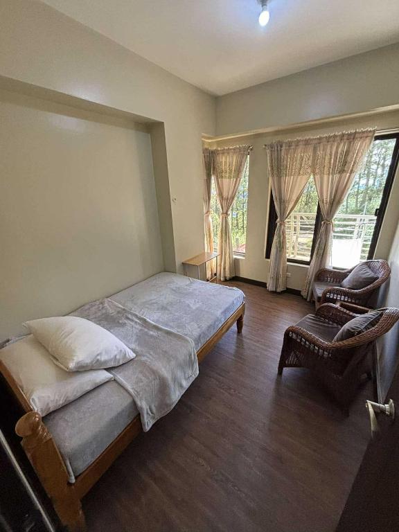 ein Schlafzimmer mit einem Bett und einem Stuhl und Fenstern in der Unterkunft Outlook Ridge Residences VY in Baguio City