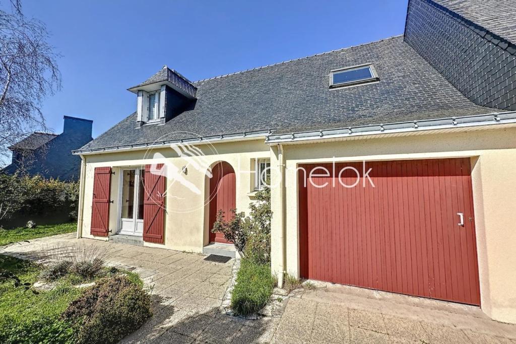 a house with red garage doors on a driveway at Maison de vacances tout confort - À 100m de la mer in Port-Louis