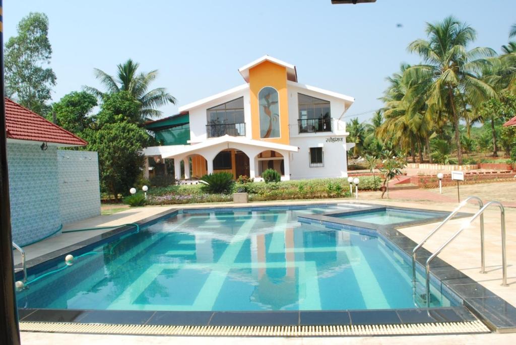 a house with a swimming pool in front of a house at Sneha Farm House in Kudāl