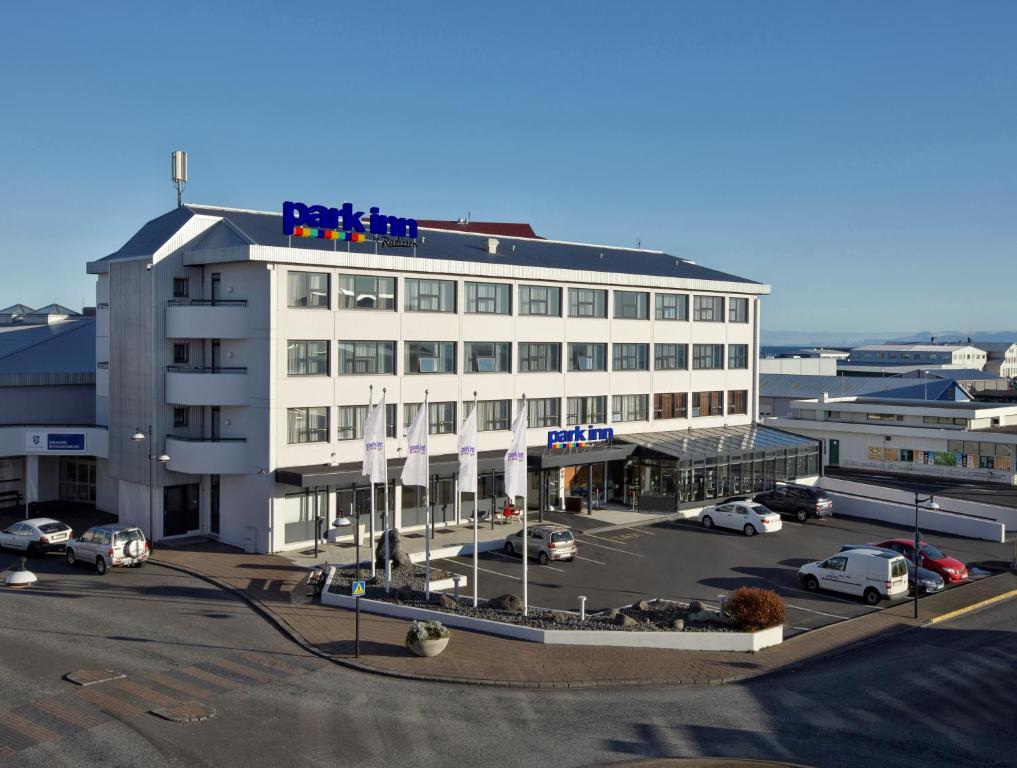 een groot wit gebouw met veel auto's op een parkeerplaats bij Park Inn by Radisson Reykjavik Keflavík Airport in Keflavík
