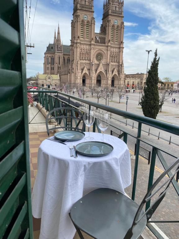 a table with wine glasses on a balcony with a cathedral at Balcon de la virgen in Luján