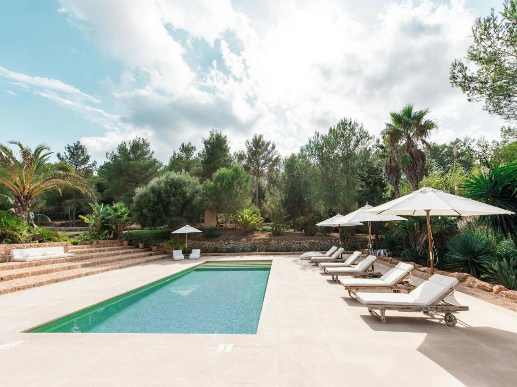 a swimming pool with lounge chairs and umbrellas at Holiday home with wooden-beamed patio in Santa Gertrudis de Fruitera