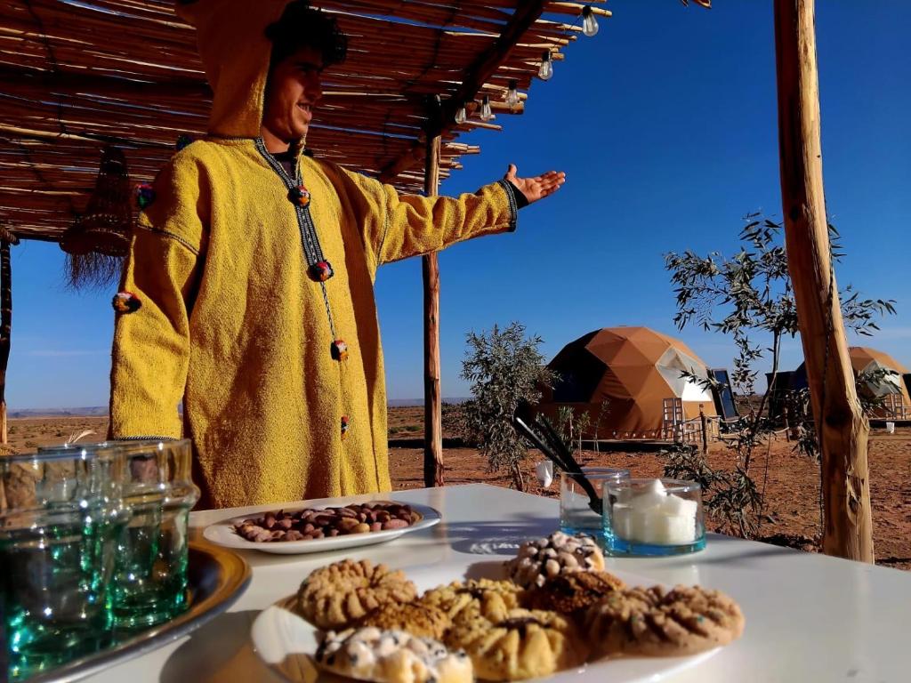 un hombre parado frente a una mesa con comida en Chic Boheme Camp, en Merzouga