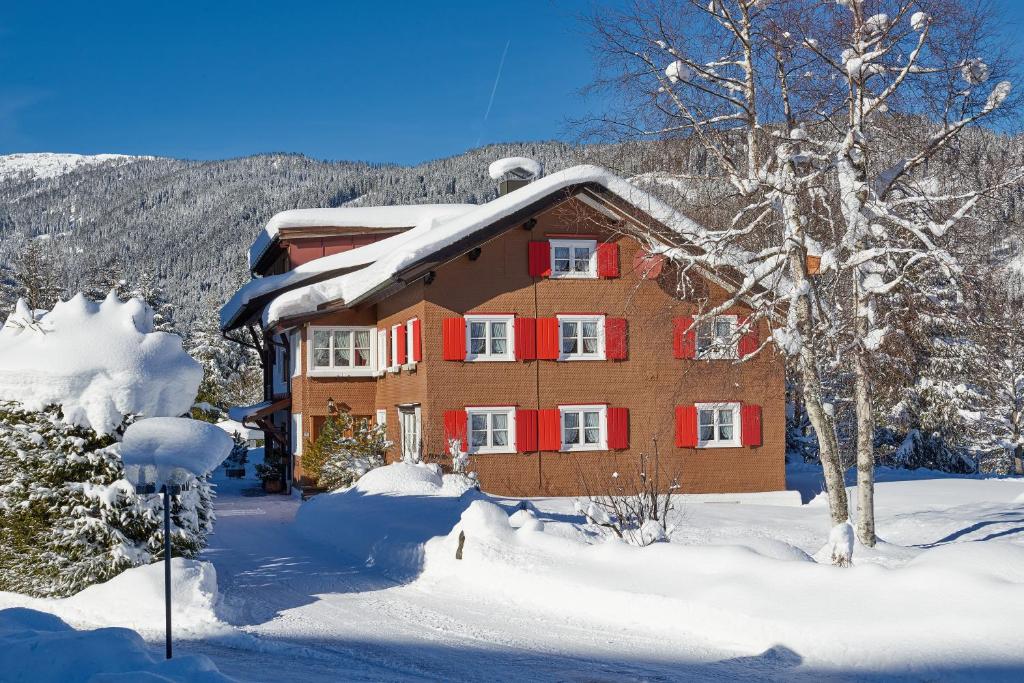 una casa cubierta de nieve con persianas rojas en Ferienhaus Kessler, en Riezlern