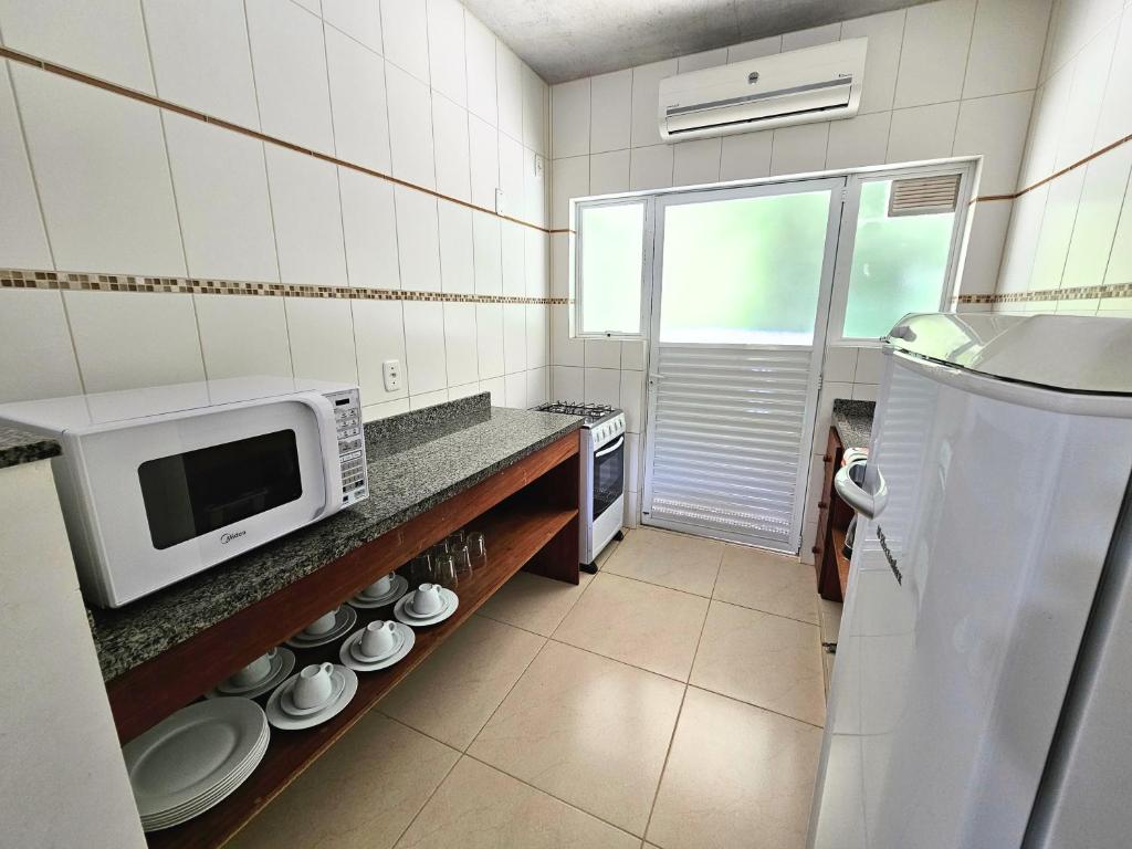 a kitchen with a microwave on a counter with plates at Refúgio da Lagoinha - Centro de Bombinhas in Bombinhas