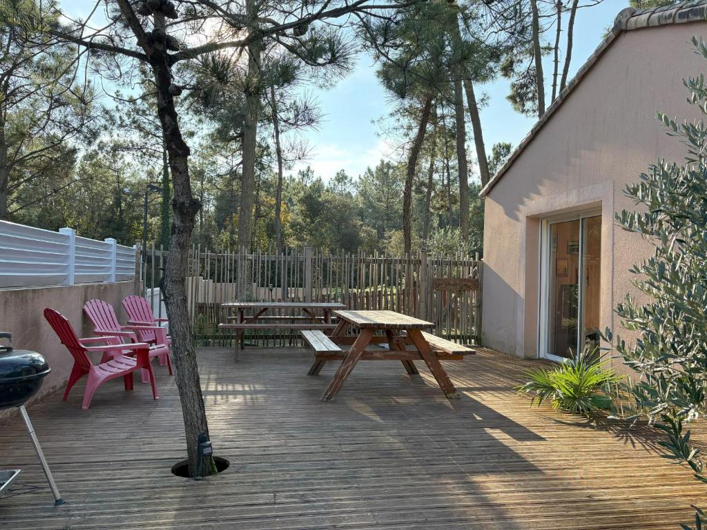 une terrasse en bois avec une table de pique-nique et des chaises dans l'établissement Maison aux portes de la forêt avec piscine privée, Wi-Fi et animaux admis - FR-1-323-558, à Saint-Jean-de-Monts