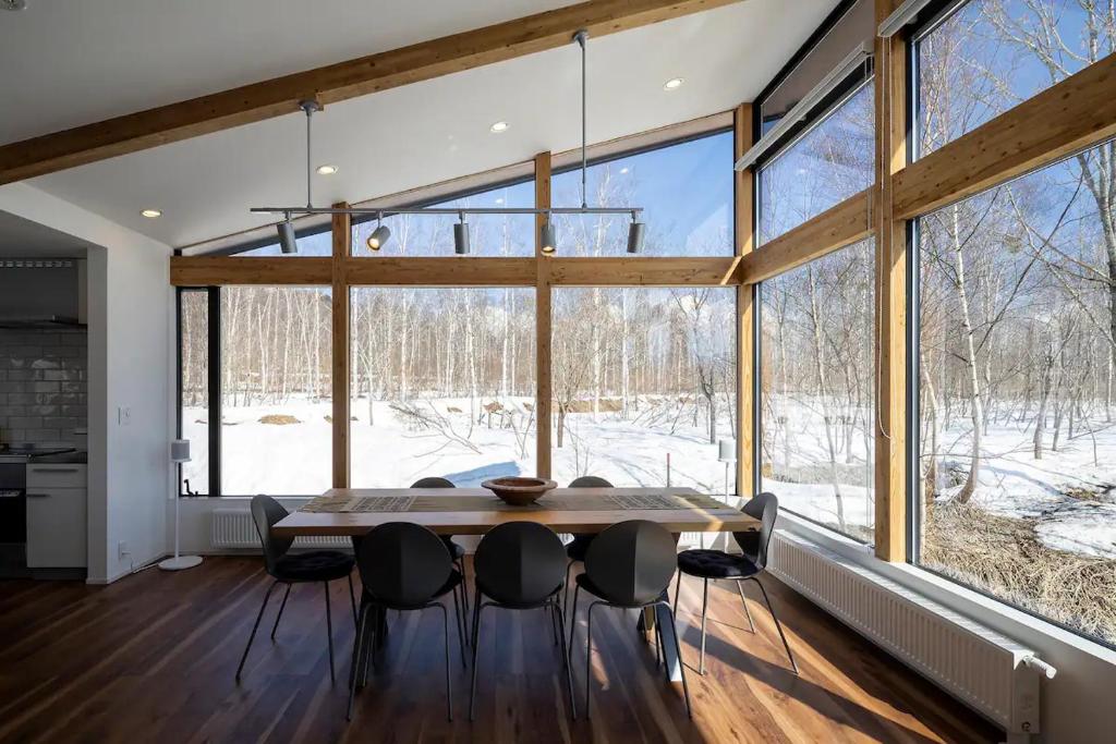 ein Esszimmer mit Tisch und Stühlen und großen Fenstern in der Unterkunft Niseko Kizuna Lodge in Niseko