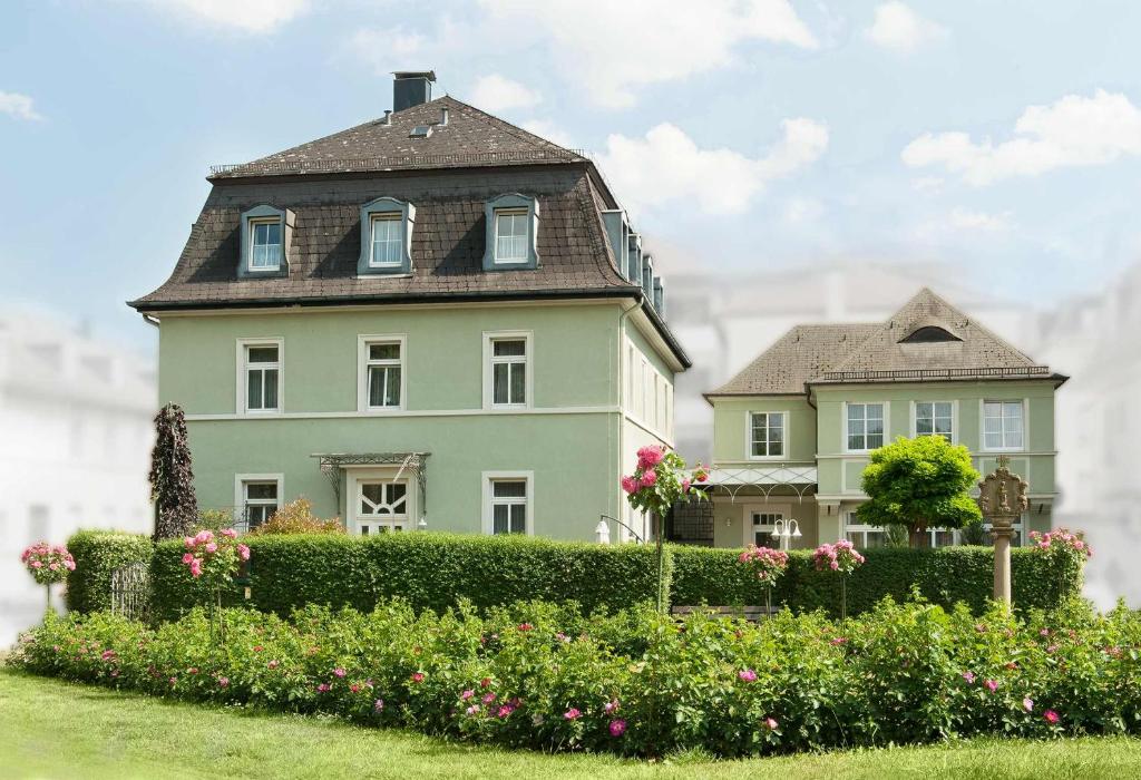 une grande maison avec une haie verte et des fleurs dans l'établissement Pension Villa Nordland, à Bad Kissingen