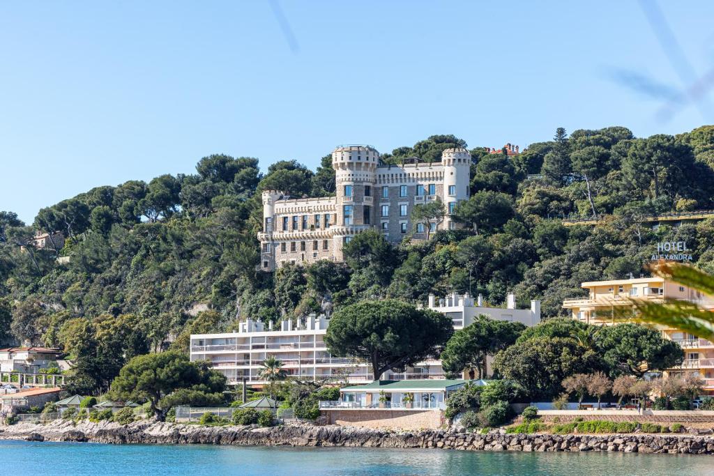 un grand bâtiment sur une colline à côté de l'eau dans l'établissement LE CHÂTEAU - La Perle du Cap Martin, à Roquebrune-Cap-Martin