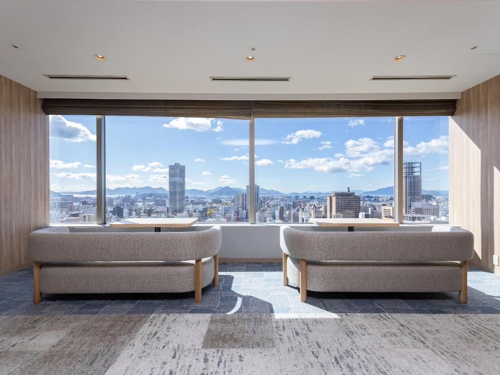 a room with two chairs and a large window at Mitsui Garden Hotel Hiroshima in Hiroshima