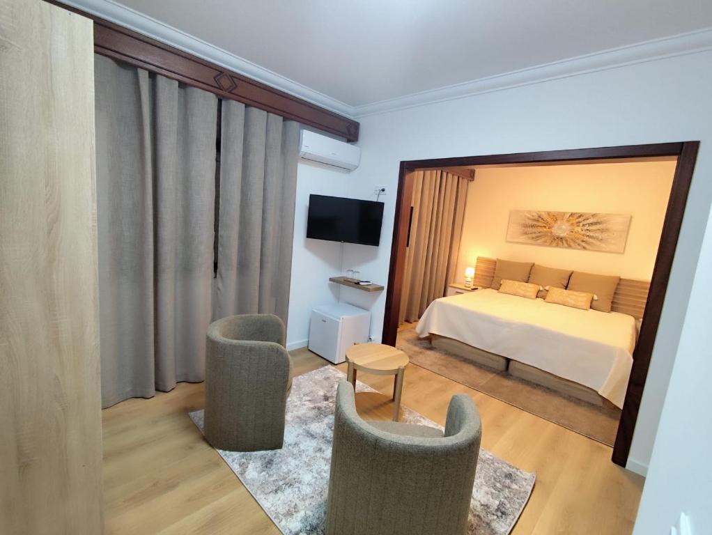 a bedroom with a bed and two chairs and a television at Residencial Pôr do Sol in Couço