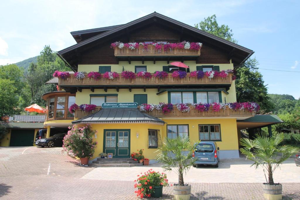 a yellow building with a balcony with flowers on it at Seepension Neubacher KG in Nussdorf am Attersee