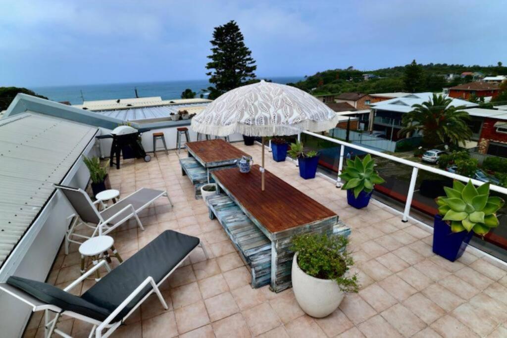 a patio with a table and chairs and an umbrella at Norah Head Beachside living with Private rooftop in Norah Head