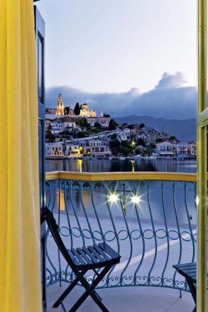 a balcony with a chair and a view of a city at Nireus Hotel in Symi