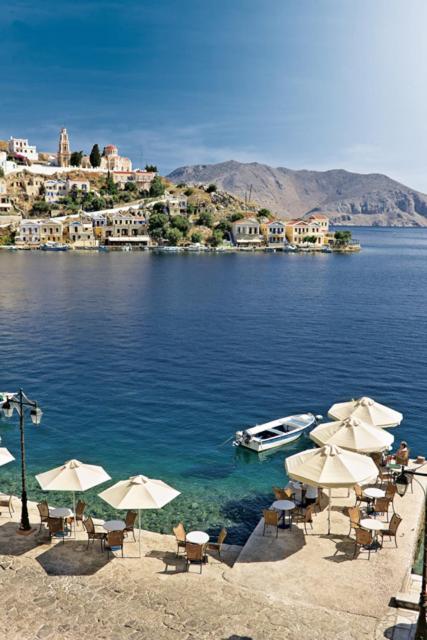 a beach with umbrellas and a boat in the water at Nireus Hotel in Symi