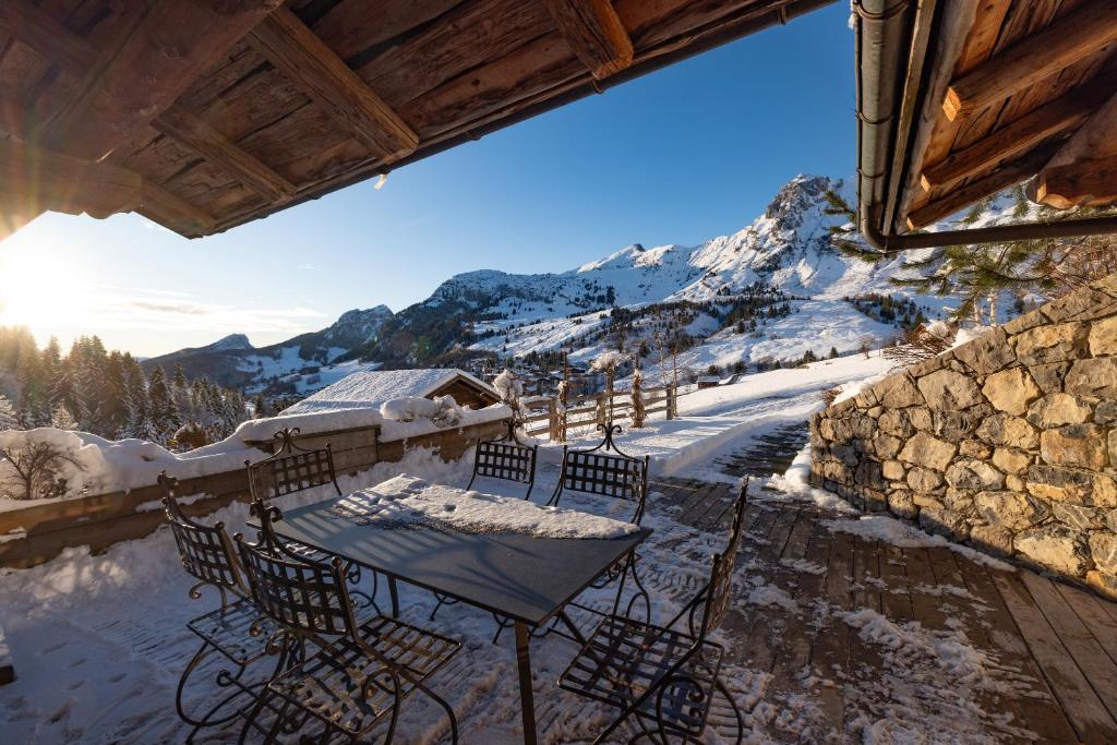 una mesa y sillas en un balcón con montañas cubiertas de nieve en Coeur de neige 1724, en Le Grand-Bornand