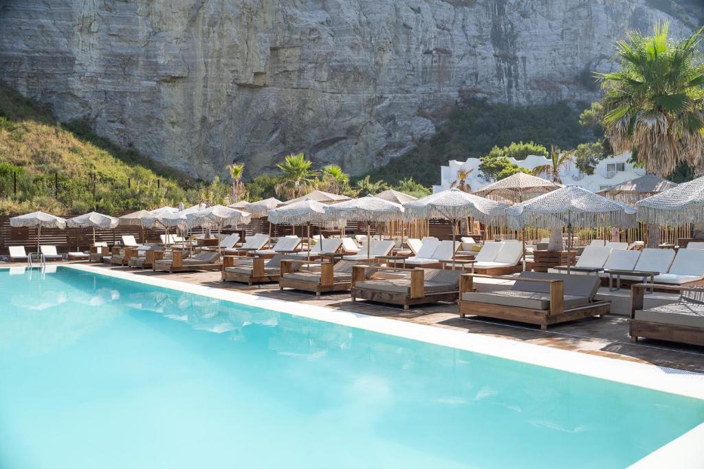 a pool with chairs and umbrellas next to a mountain at Maya Beach Resort in Massa Lubrense