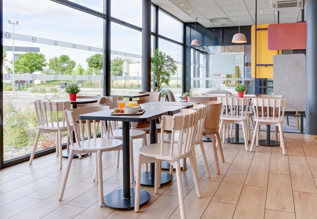 Una mesa y sillas en un restaurante con ventanas. en B&B HOTEL Reims Croix Blandin, en Reims