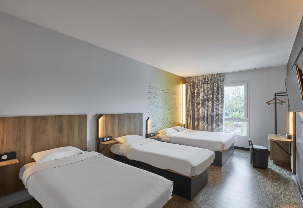 a hotel room with three beds and a window at B&B HOTEL Ouistreham in Ouistreham