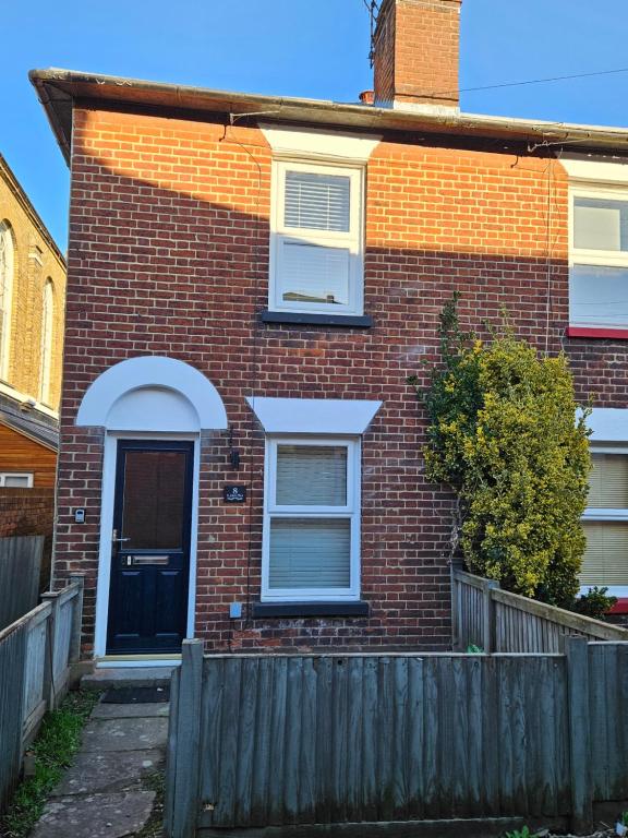 een stenen huis met een zwarte deur en een hek bij Pretty City Centre Cottage in Hackington