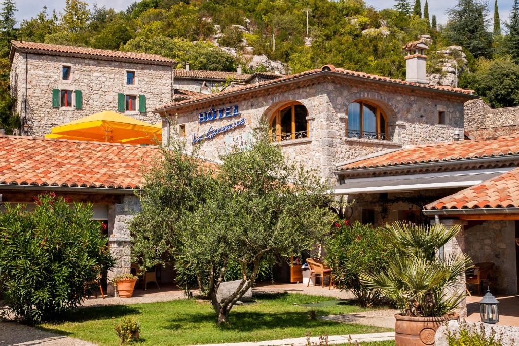 un grande edificio in pietra con alberi di fronte di Hôtel La Garenne a Labeaume