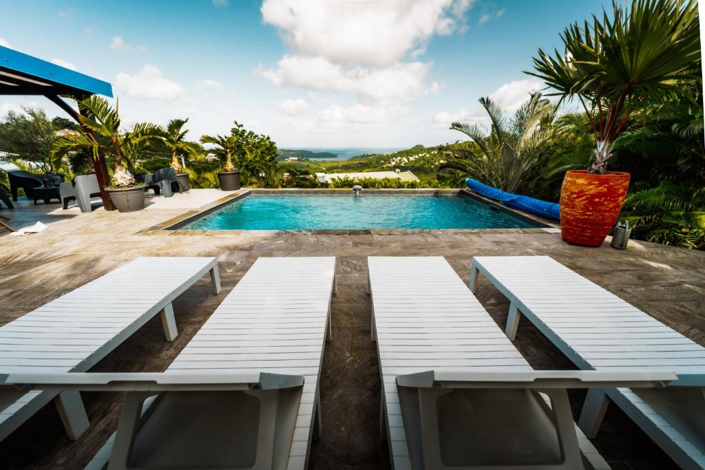 una piscina con due panche bianche in un resort di Bas de villa le rêve éveillé a Le Robert