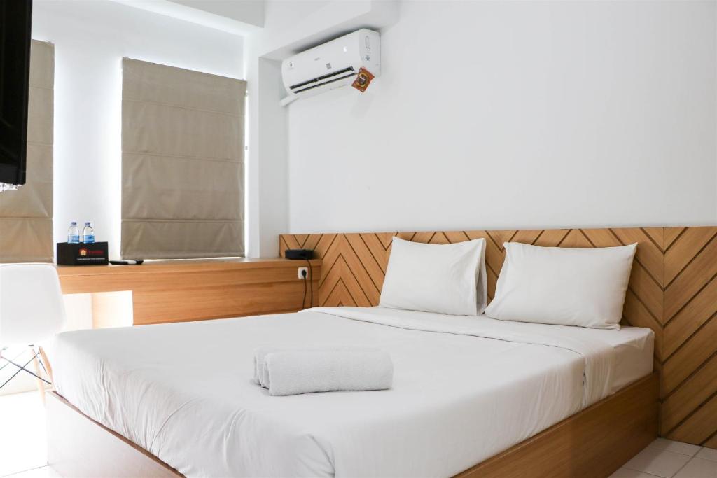 a bedroom with a white bed with a wooden headboard at Minimalist and Cozy 1BR Patraland Urbano Apartment By Travelio in Bekasi