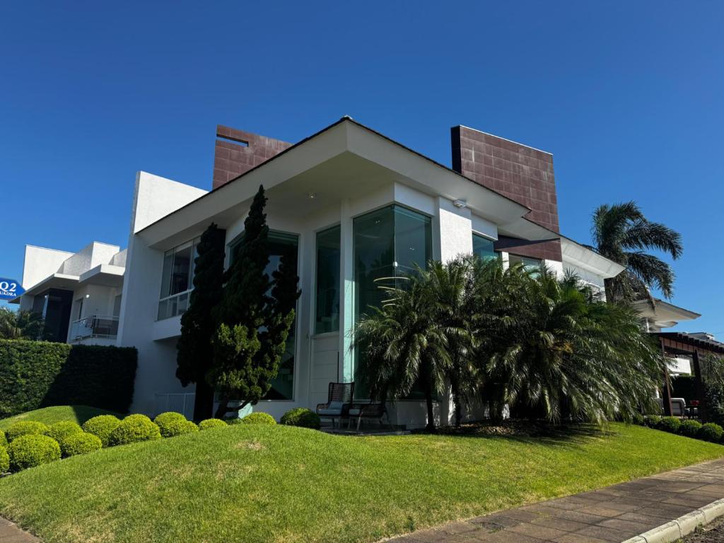 a white house with palm trees in front of it at Casa Luxuosa no Condomínio Condado de Capão in Capão da Canoa