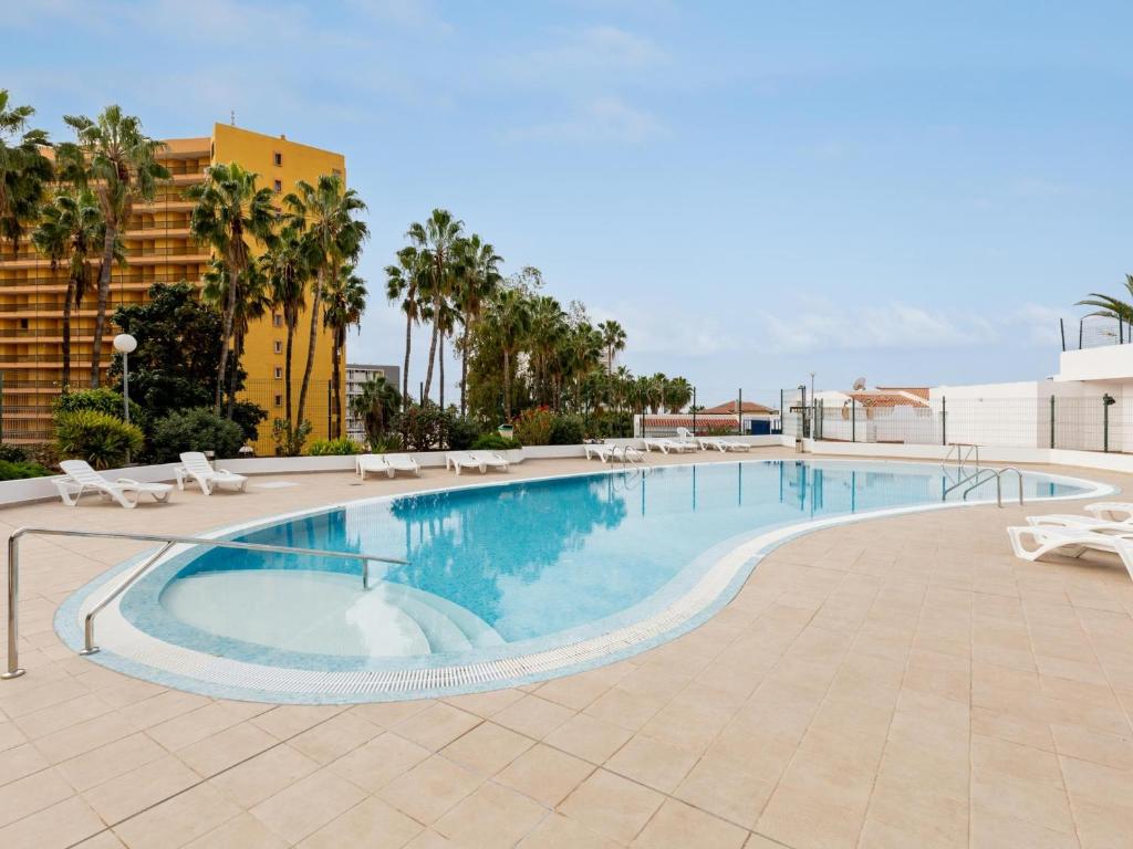 a large swimming pool with white chairs and palm trees at 1H mediterran flores apartment in Costa de Adeje