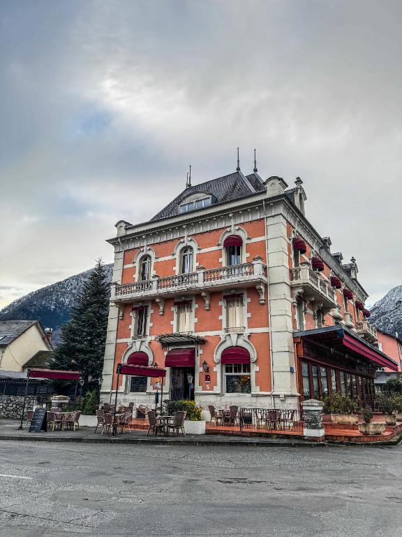 un grand bâtiment en briques avec des tables et des chaises devant lui dans l'établissement Grand Hôtel de France, à Pierrefitte-Nestalas