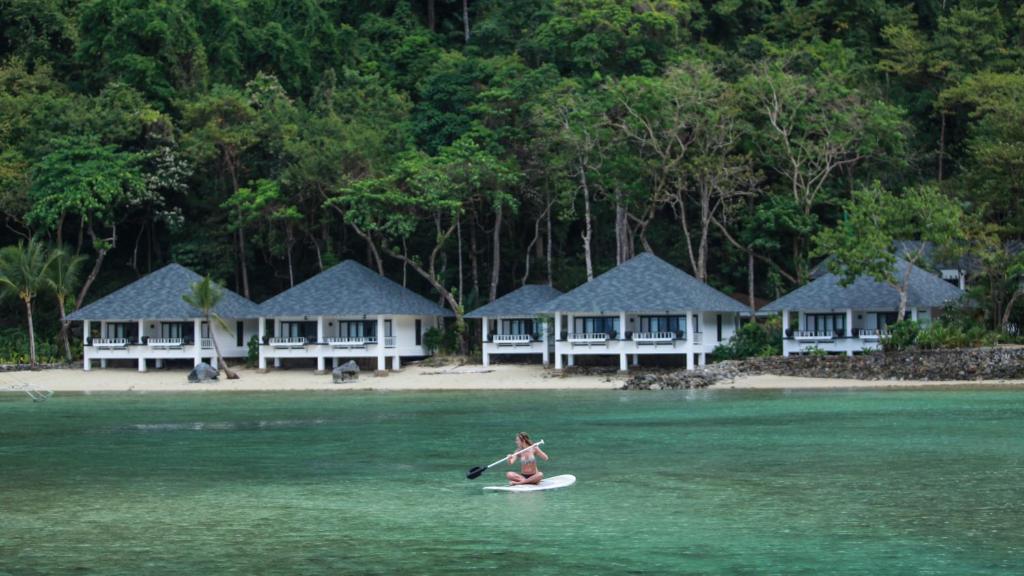 a woman is riding a surfboard in the water at El Nido Resorts Lagen Island in El Nido