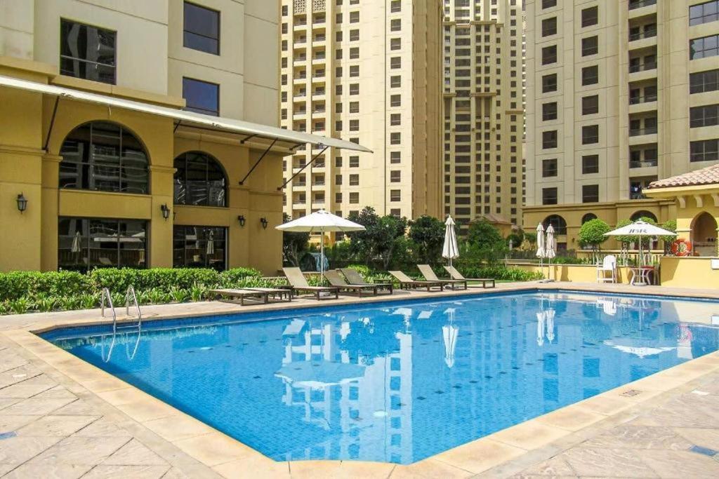 a large swimming pool with chairs and buildings at TWIN BED-ROOM Sadaf Community near TRAM in Dubai