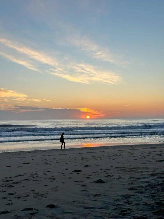 una persona caminando por la playa al atardecer en Située a 3 minutes de la plage, en Yof