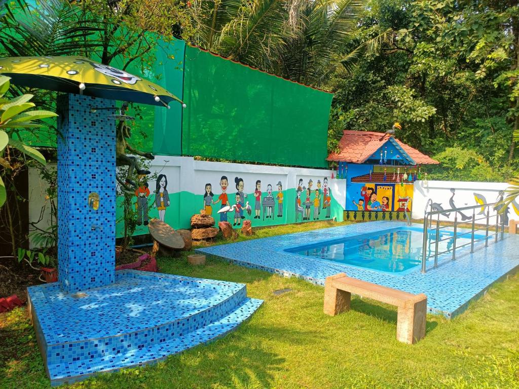 a small swimming pool with an umbrella and a playground at Rimzim's Tatvamasi - You In Nature in Kudal